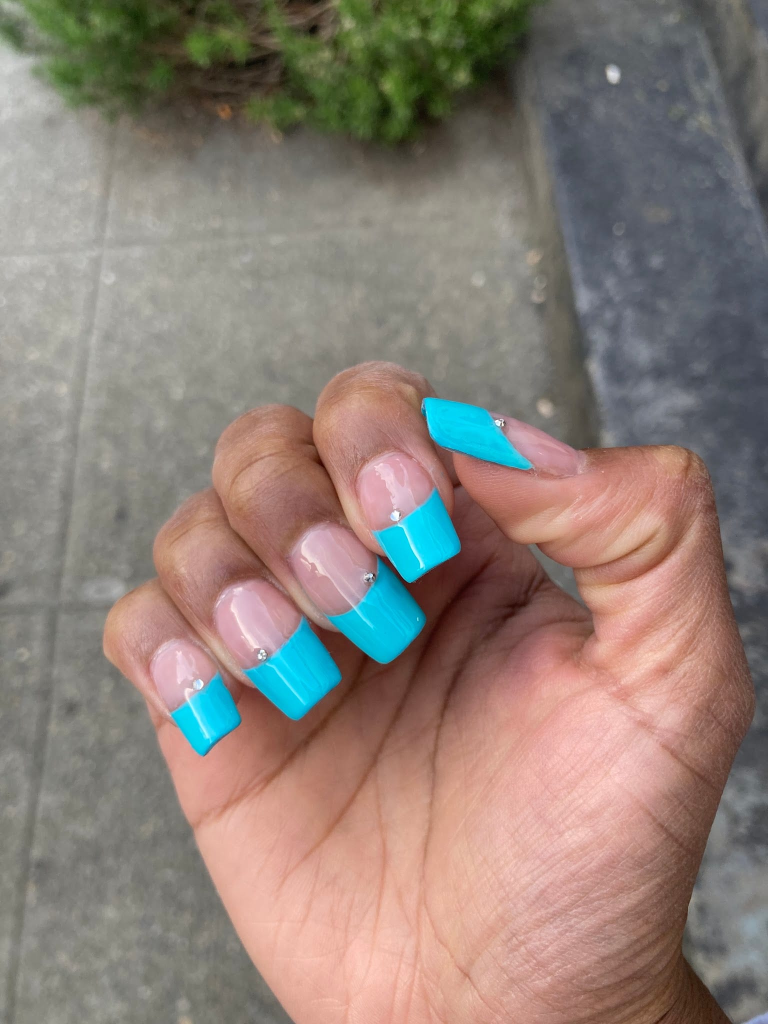 Hand with turquoise French tip acrylic nails and small rhinestone accents