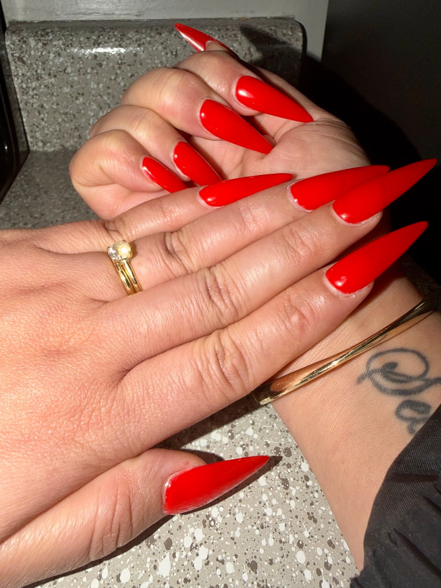Long red stiletto acrylic nails on two hands with gold jewelry