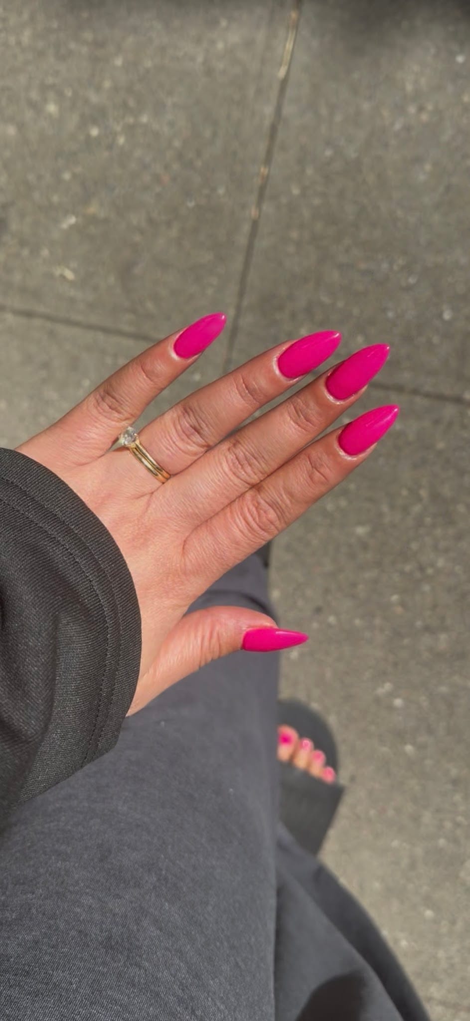 Hand with long almond-shaped hot pink acrylic nails and gold ring