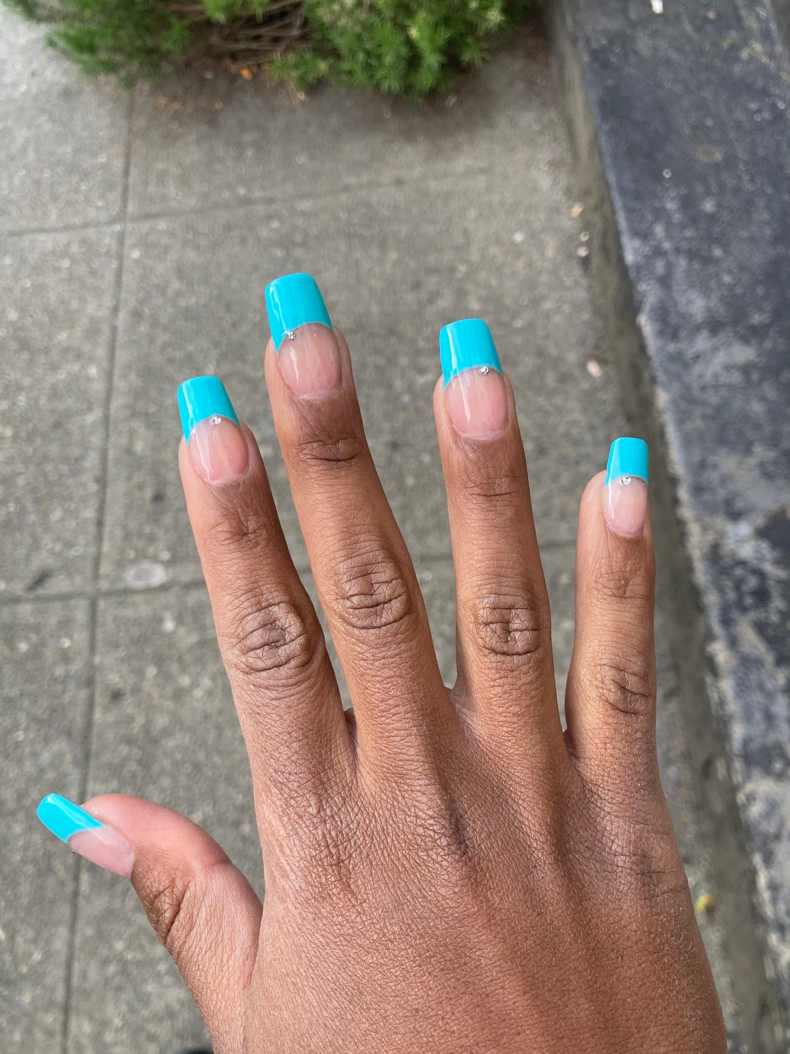 Hand with long square acrylic nails featuring teal French tips and rhinestones
