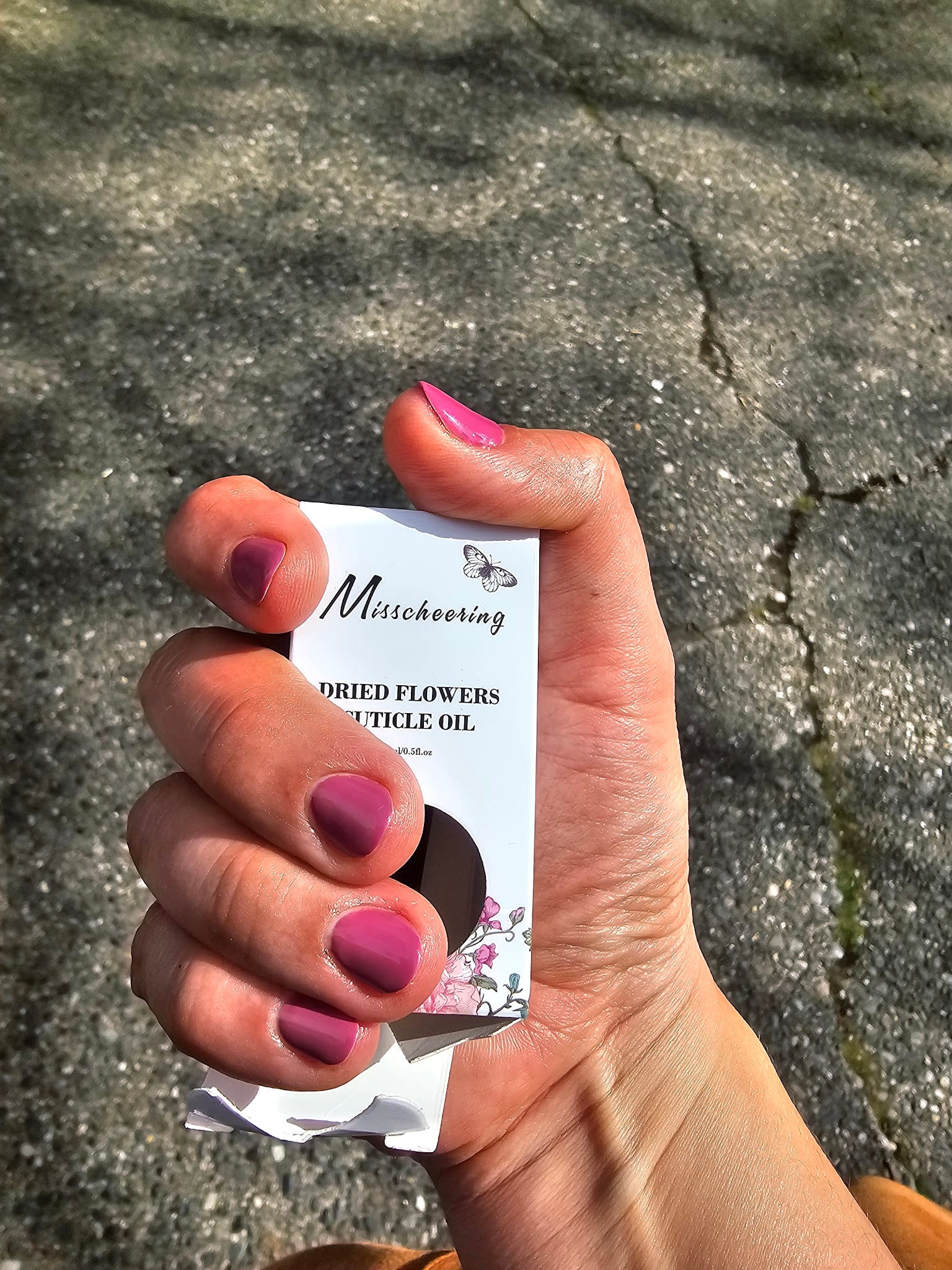 Hand with mauve gel nails holding Misscheering dried flowers cuticle oil box