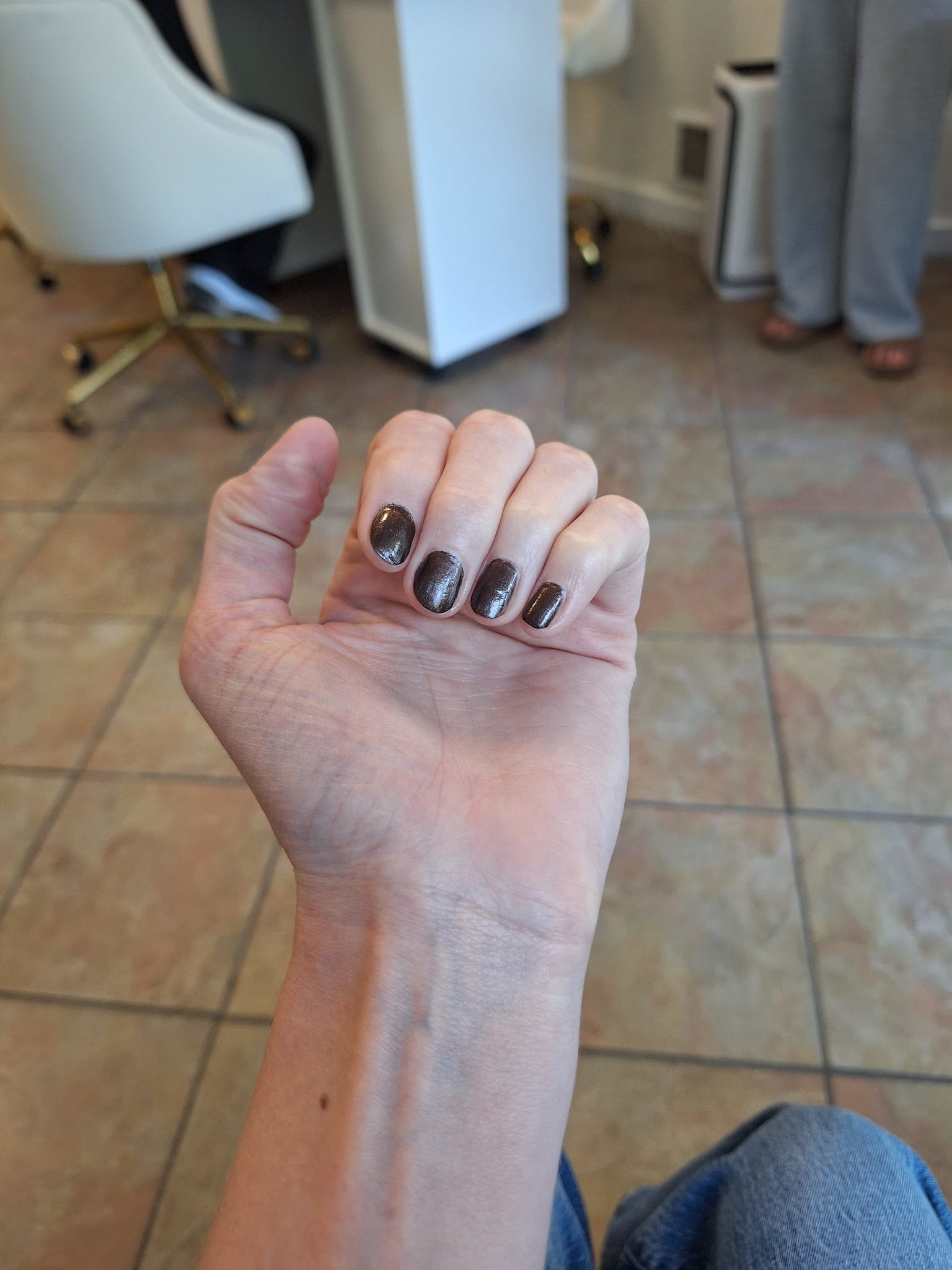 Hand with short nails painted in dark brown gel polish at nail salon.
