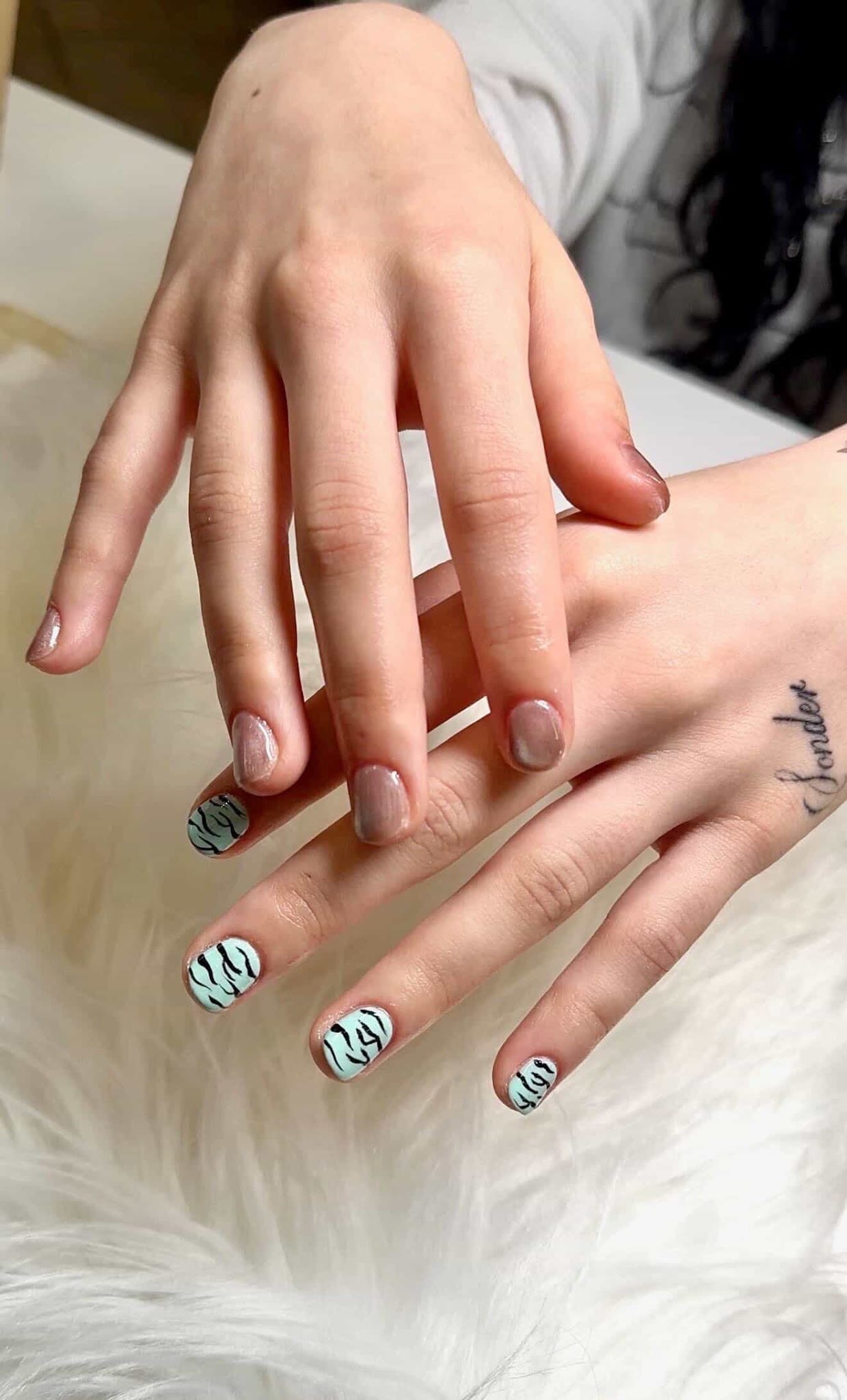 Two hands showing nude gel nails with mint zebra print nail art accents