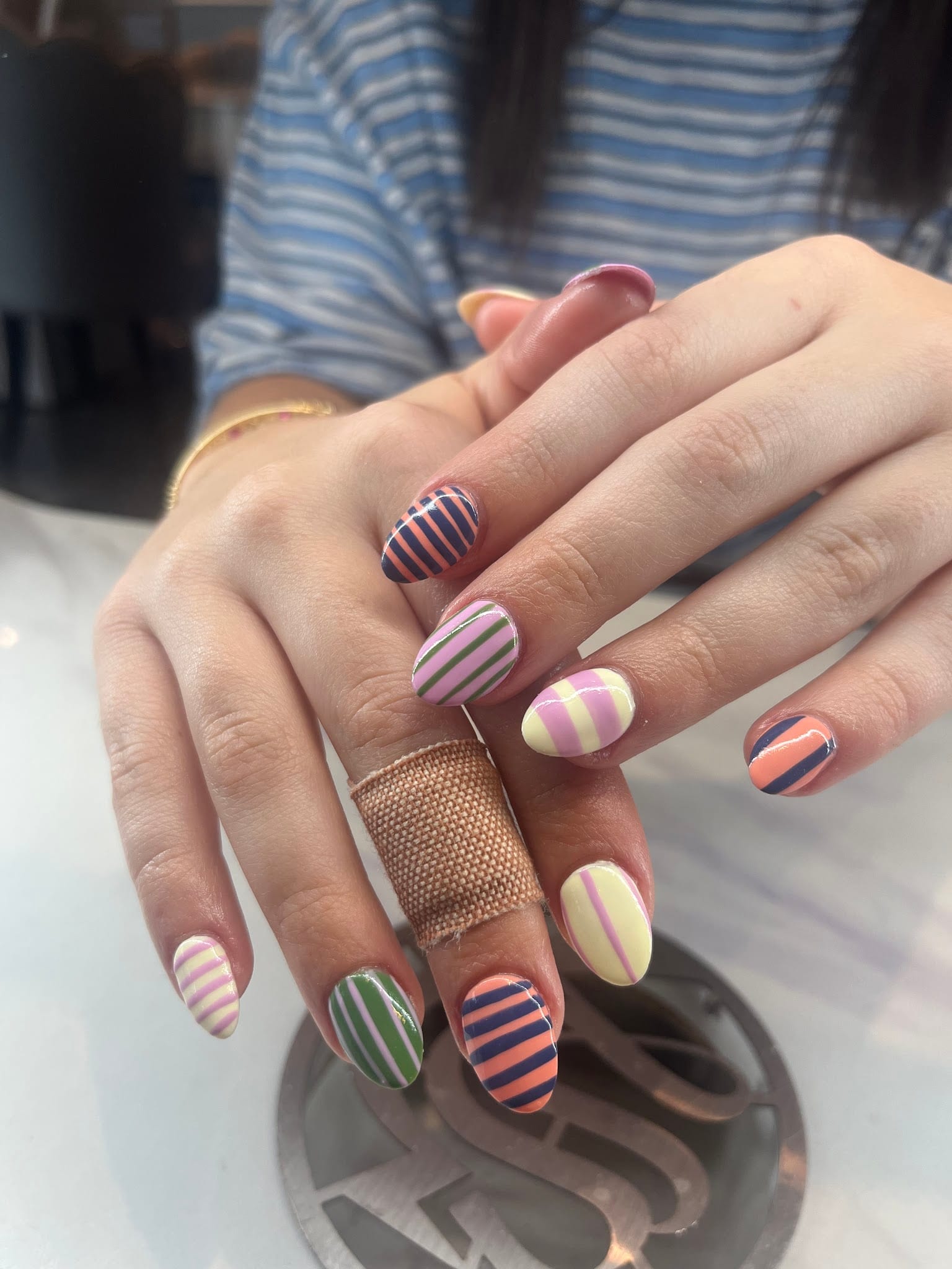 Two hands with colorful striped nail art in pink, orange, navy, green, and yellow