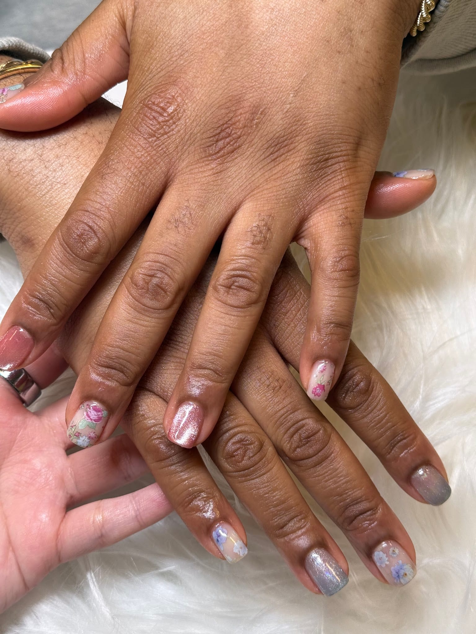 Two hands displaying short nails with pastel floral nail art designs